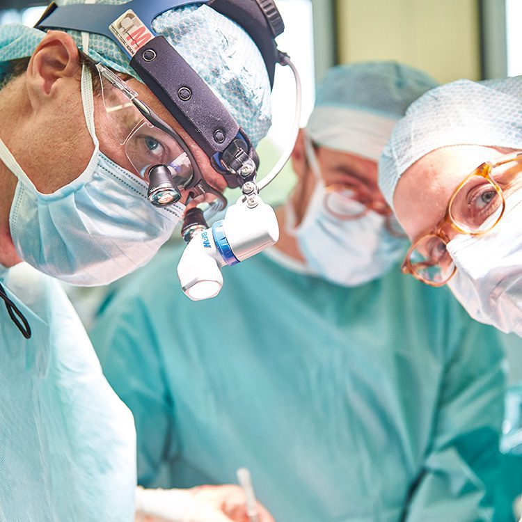 OP-Situation, drei Personen in grüner OP-Arbeitskleidung während einer Operation