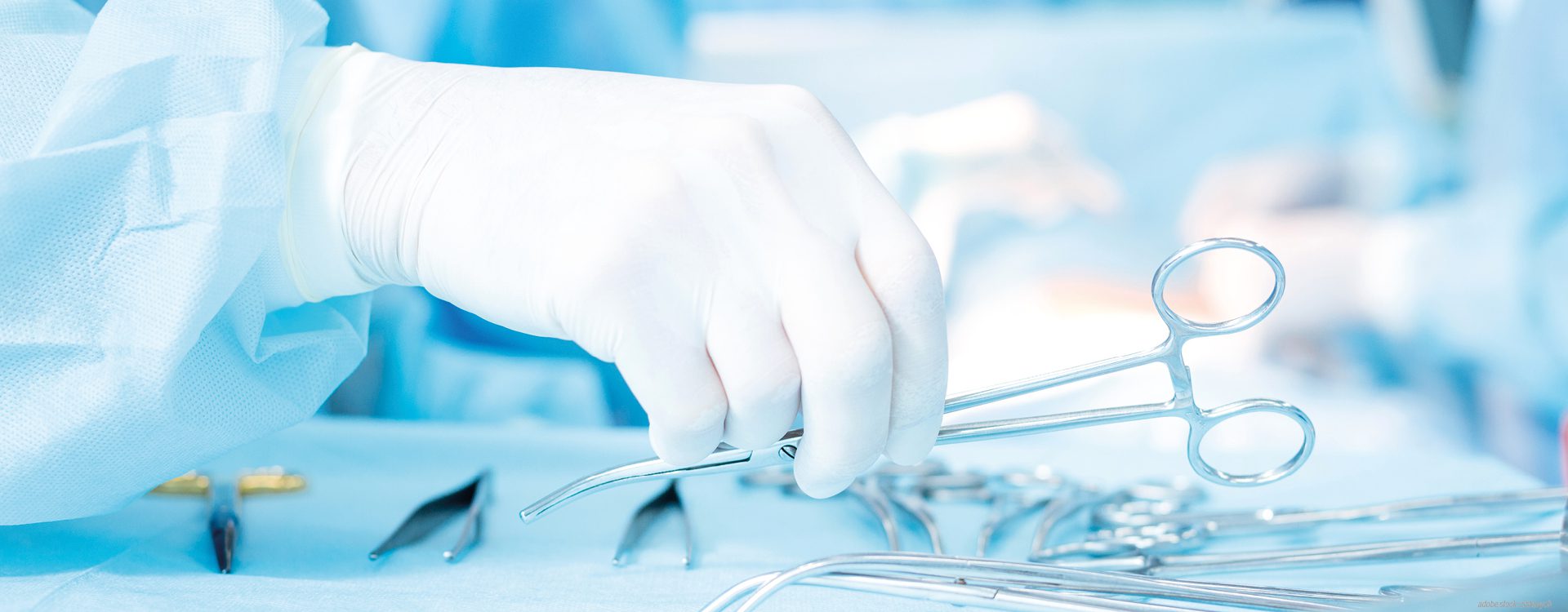 Behandschuhte Hand die ein Operationsinstrument von einem Tisch mit weiteren medizinischen Instrumenten nimmt.