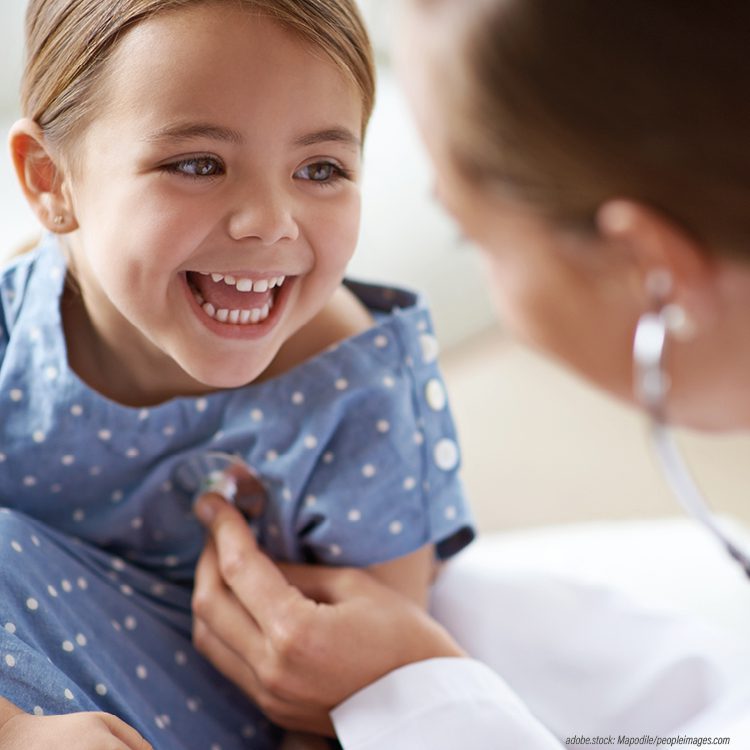 Etwa vierjähriges Mädchen mit Zöpfen lächelt ihren behandelnden Arzt an.