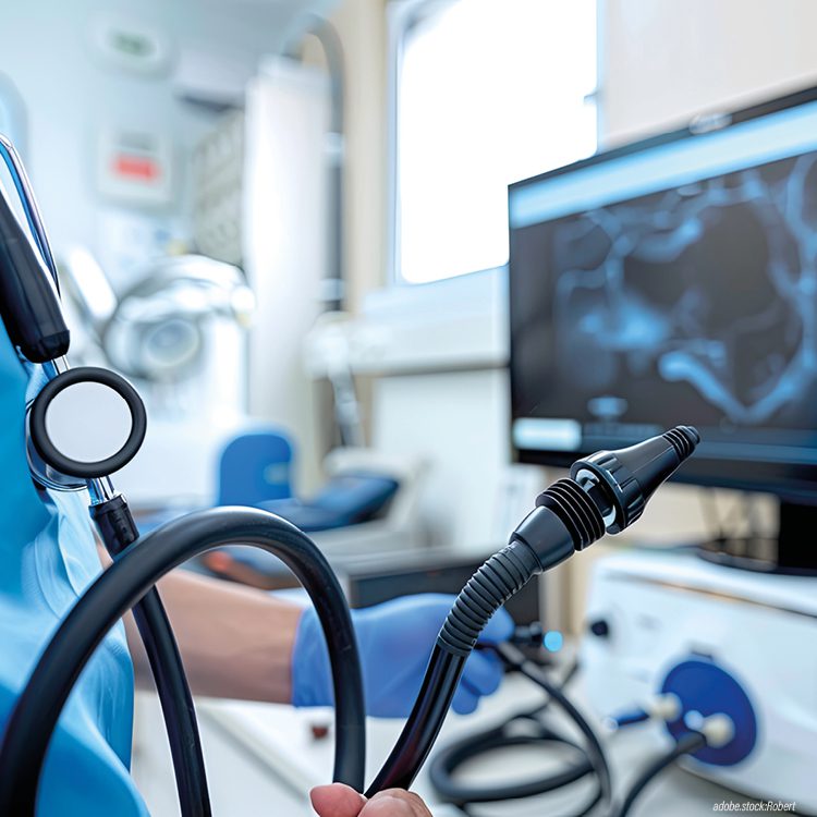 Person in bleuer Krankenhausarbeitskleidung mit Gastroskop betrachtet ein Bild am Monitor