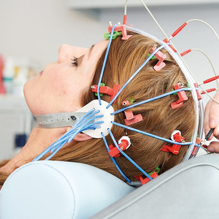 Frau während einer EEG-Untersuchung auf dem Untersuchungsstuhl mit Elektroden am Kopf