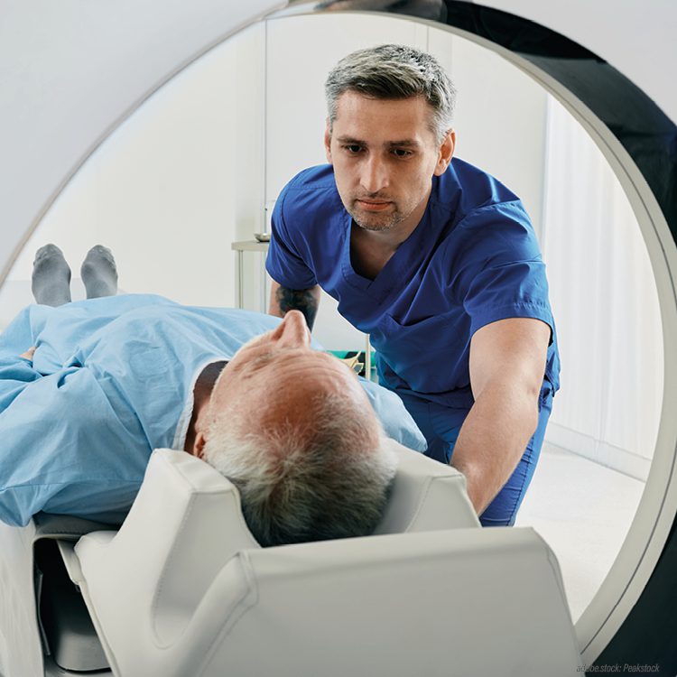eine männliche Person wird auf einer Untersuchungsliege von einer männlichen medizinischen Fachkraft in ein Computertomographiegerät geschoben
