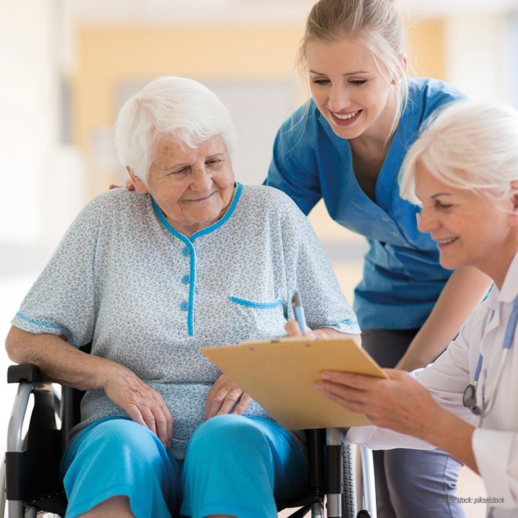 Ältere Patientin im Rollstuhl im Gespräch mit einer weiblichen Pflegekraft und einer Ärztin.
