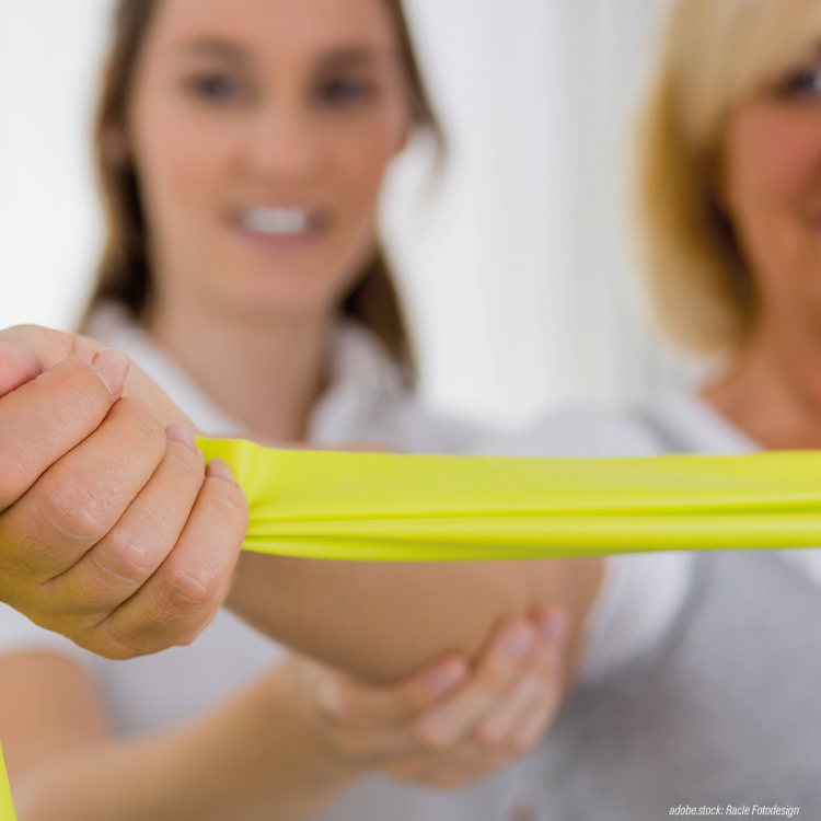 Physiotherapeutin unterstützt eine Patientin bei einer Übung mit einem gelben Gymstikband