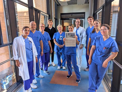 Medizinisches Team in blauen OP-Kitteln und weißen Kitteln steht stolz mit FAZ-Ranking-Urkunde in einem modernen Krankenhaus-Korridor